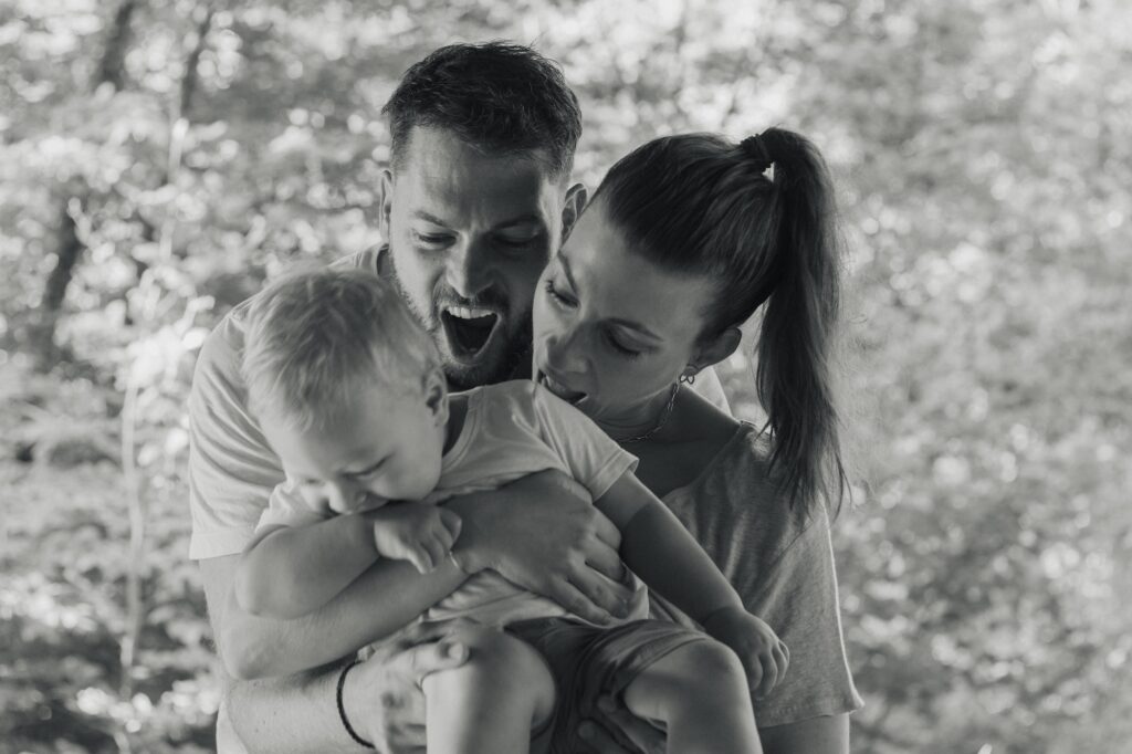 Séance photo famille complice en noir et blanc, parents et bébé en plein fou rire, Suisse romande